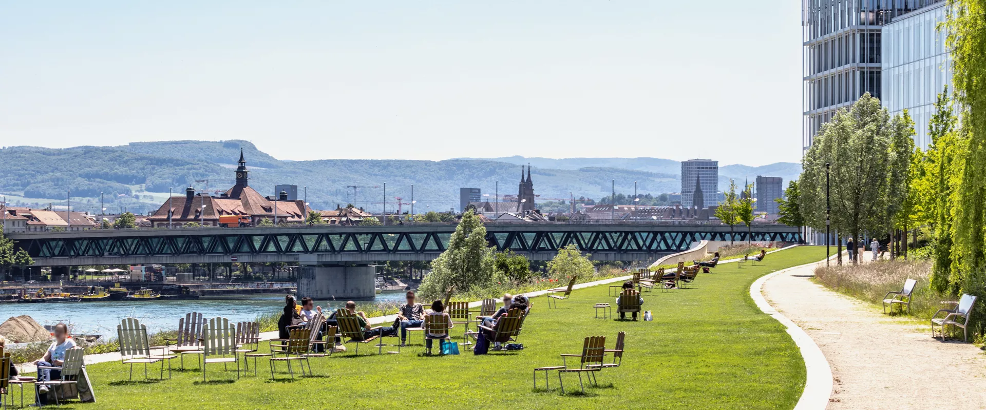 A panoramic view of Basel，from the Novartis Campus with people lounging in the foreground and the black forest in the background