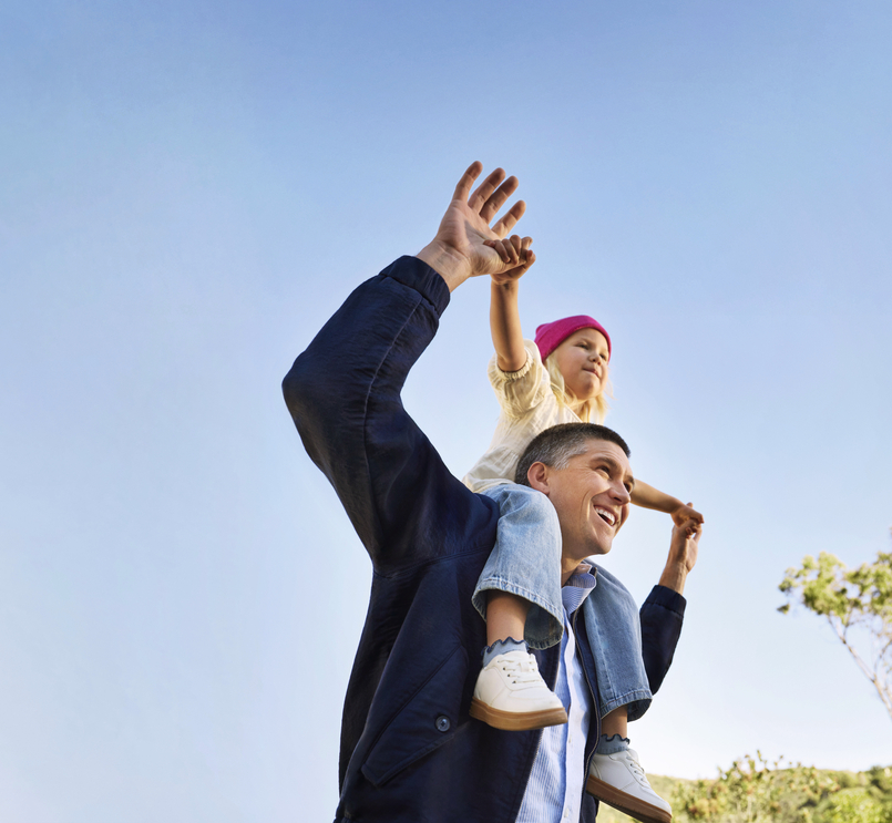 Happy parent with child on shoulders under clear sky