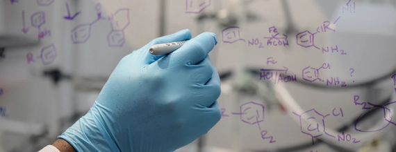 Chemist writing chemical reactions on glassboard in laboratory