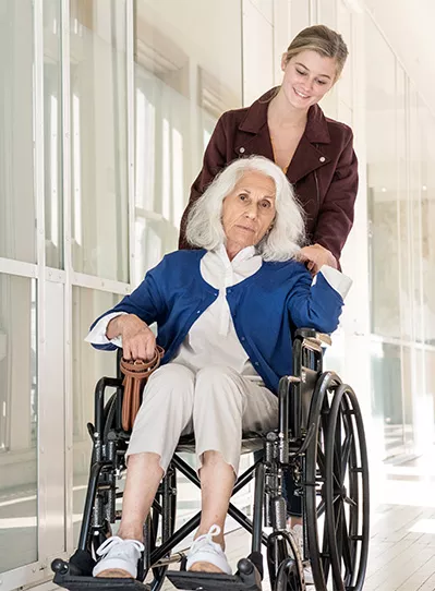 Junge Frau schiebt ältere Dame im Rollstuhl