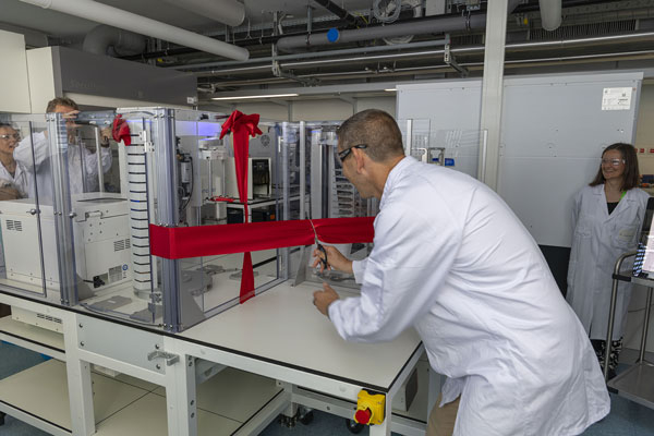 Mensch und Maschine eröffnen gemeinsam - Jon Novak beim Ribbon Cut – synchron mit dem Roboterarm des neuen Automatisierungssystems.