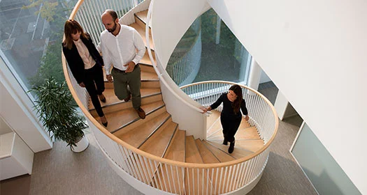 Menschen auf einer Spiraltreppe in einem modernen Bürogebäude.