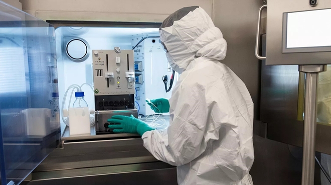 Un collaborateur portant un équipement de protection individuelle complet et utilisant des équipements spécialisés sur la ligne de production de thérapie par radioligands.