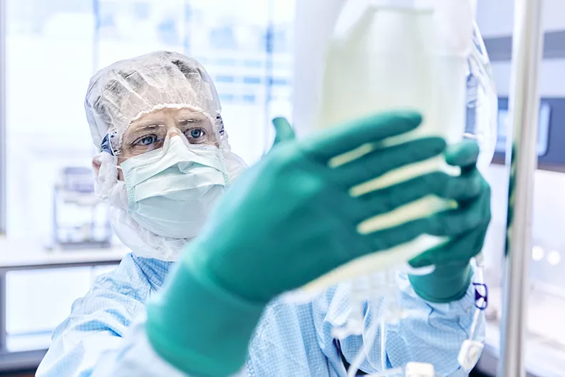 Un technicien en tenue de protection manipule une poche de liquide en laboratoire