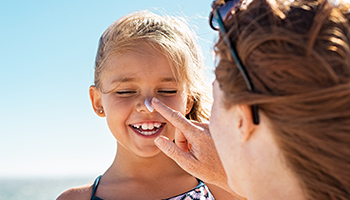 Une femme applique de la crème solaire sur le visage d'une enfant