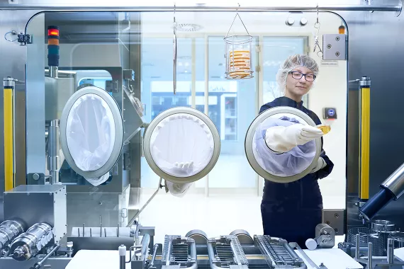 Eine Produktionsmitarbeiterin in Schutzkleidung arbeitet unter steriler Atmosphäre / Une employée de production opérant en milieu stérile