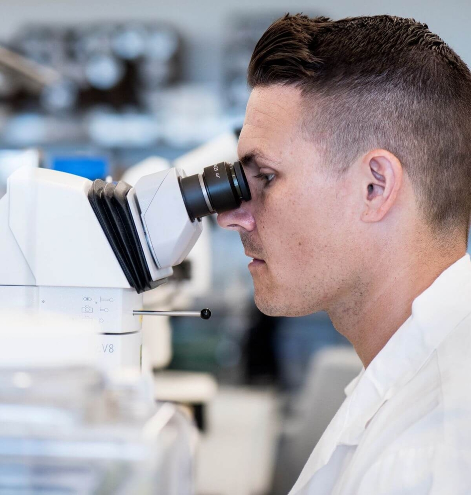Detailní pohled z profilu na laboratorního specialistu pracujícího s profesionálním mikroskopem