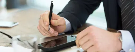 Ruce podnikatele s tužkou a mobilním telefonem