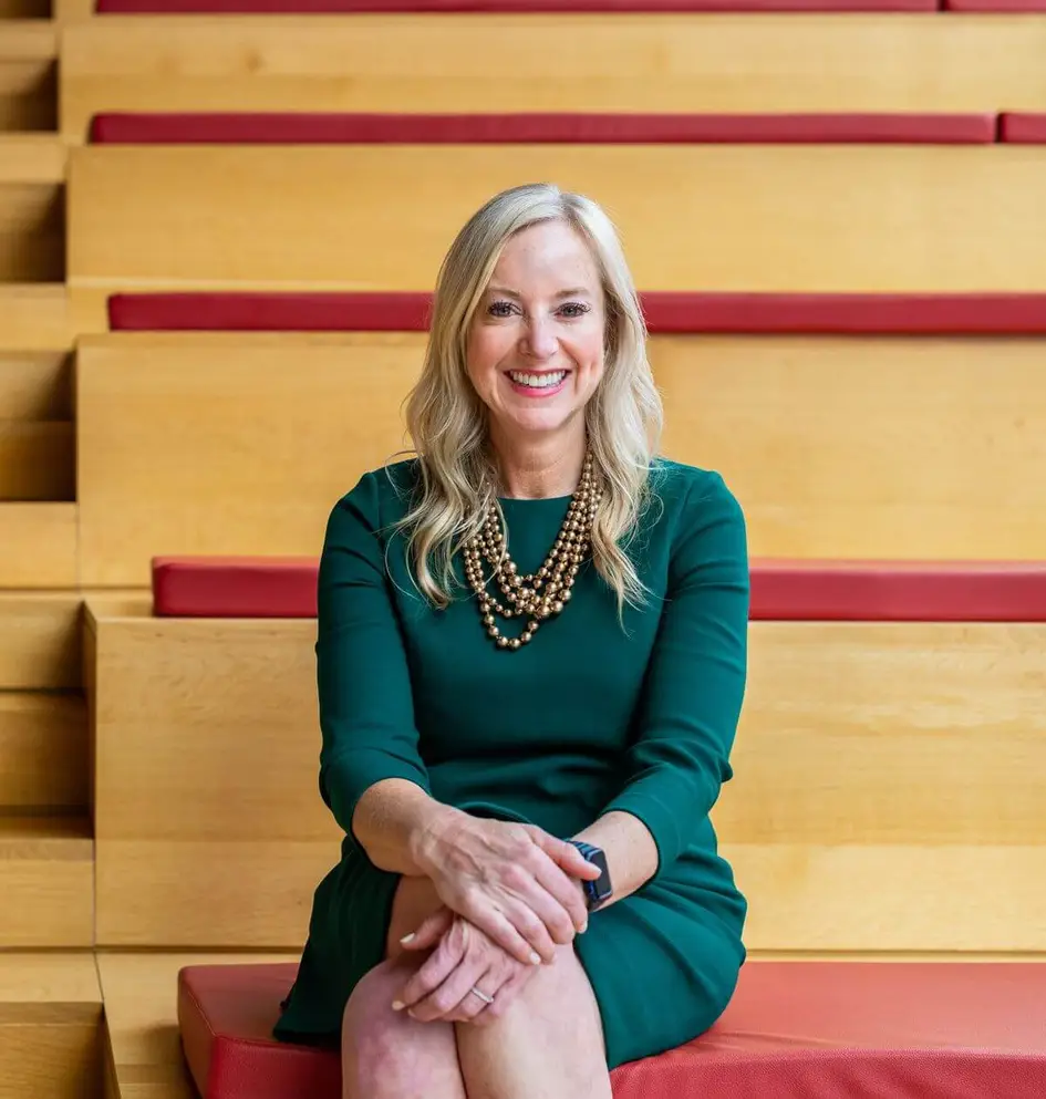 Portrait of a smiling professional woman in a green dress sitting in a modern wooden auditorium-style space