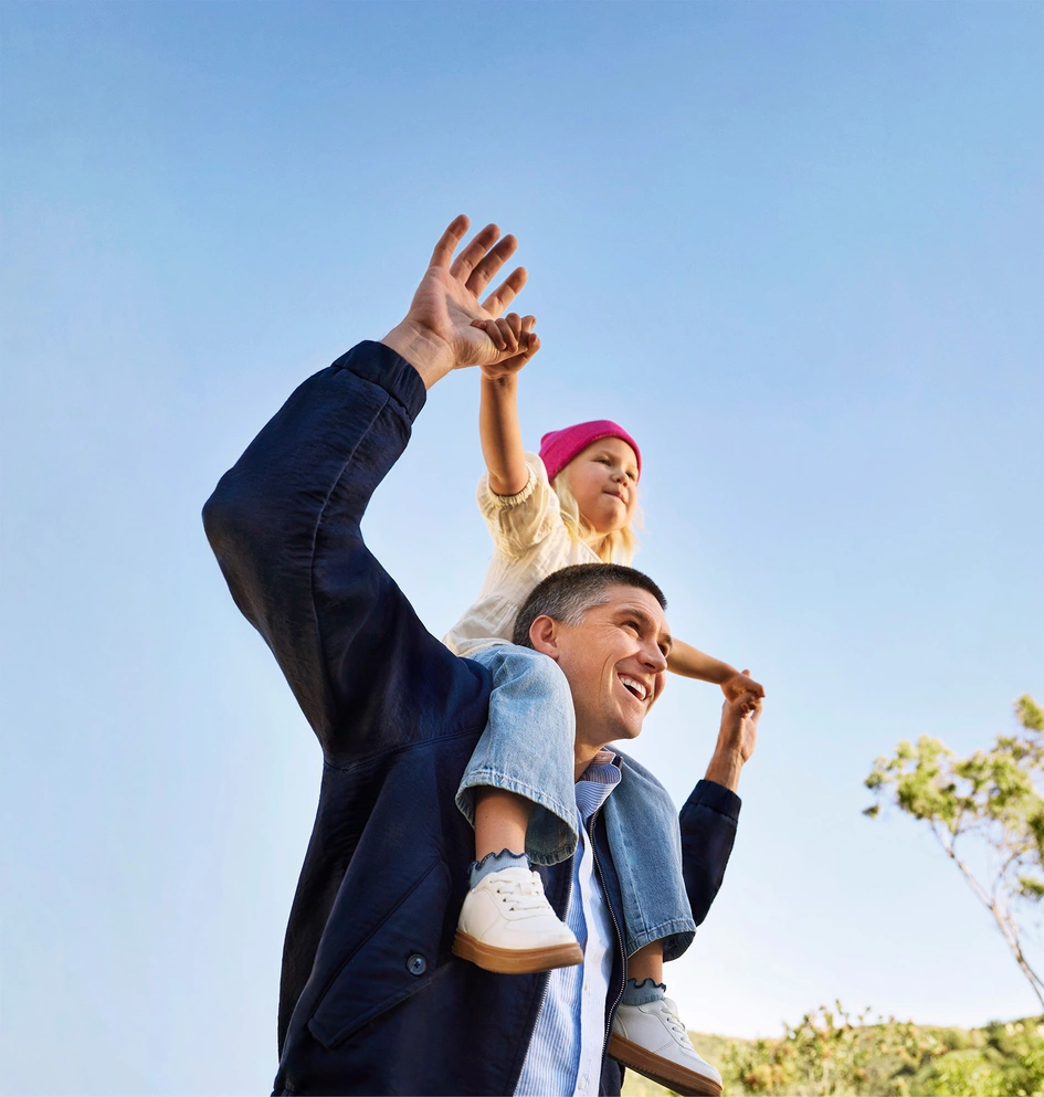 Glücklicher Vater mit Kind auf den Schultern unter blauem Himmel