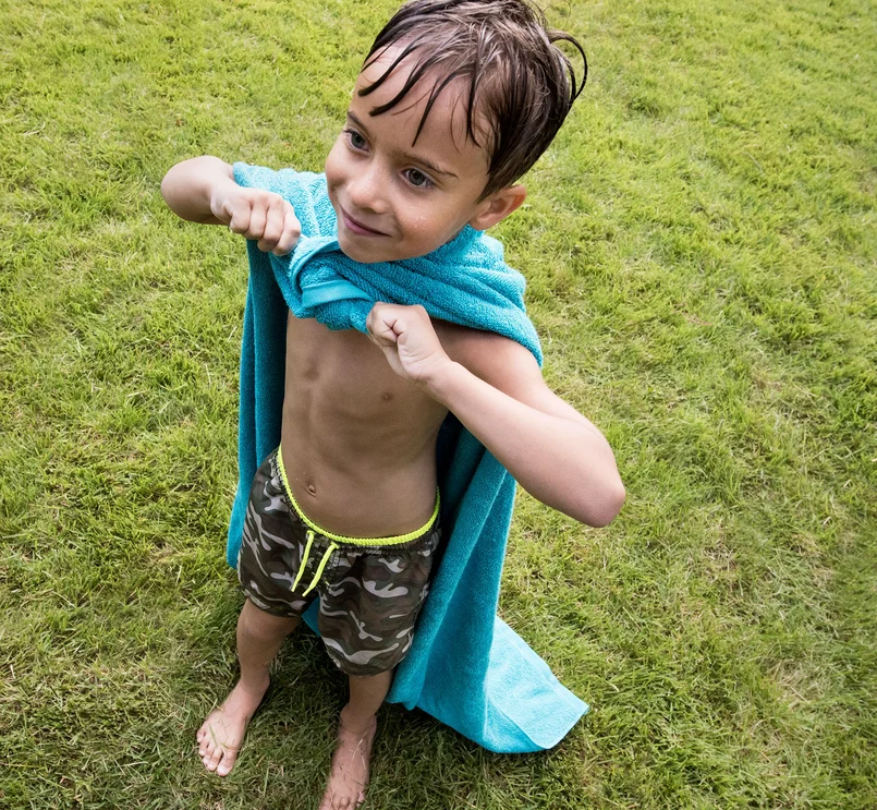 Kind spielt draußen mit einem Handtuch auf dem Gras.