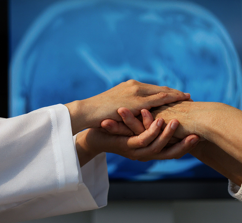 Ärzte untersuchen die Hand eines Patienten, im Hintergrund ein Gehirnscan.