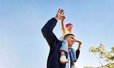 Glücklicher Vater mit Kind auf den Schultern unter einem blauen Himmel