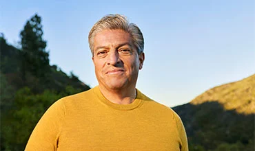 Ältere Person in gelbem Pullover draußen bei Sonnenuntergang.