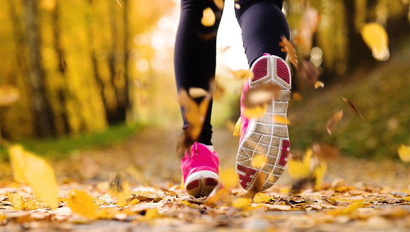 Nahaufnahme der Schuhe einer joggenden Person im Herbstlaub