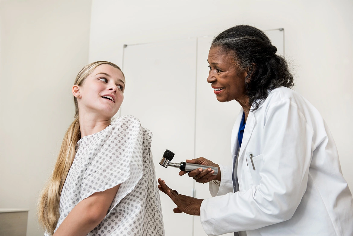 Eine Frau in einem OP-Hemd blickt zu einer anderen Frau in einem weißen Kittel, die ein medizinisches Gerät in der Hand hält.