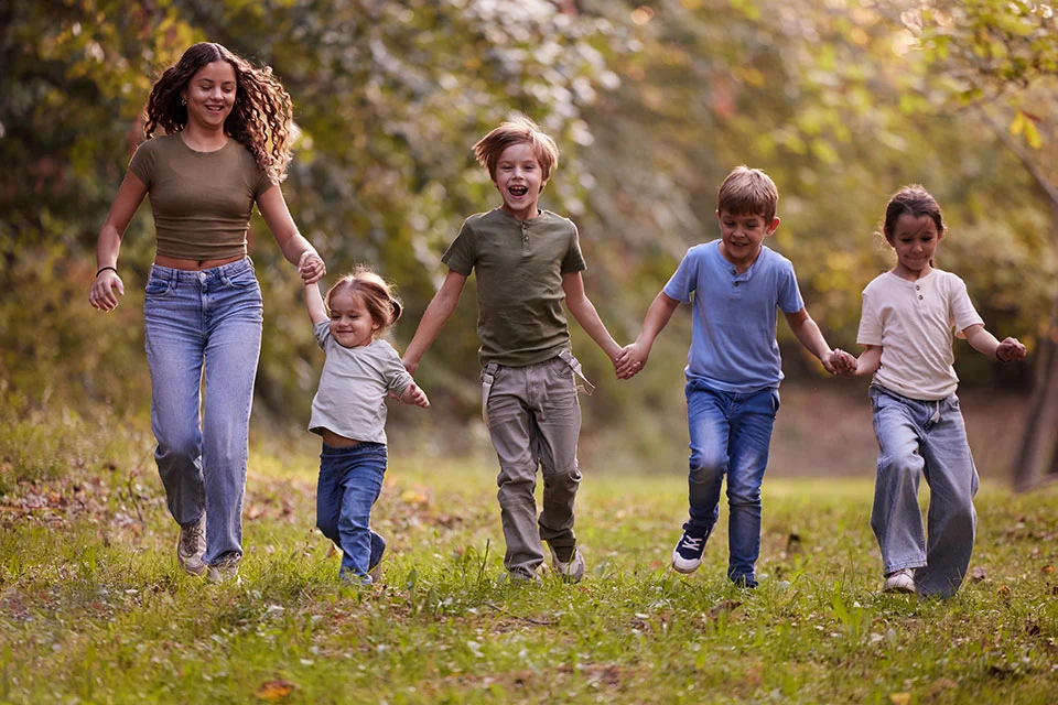 Fünf Kinder im unterschiedlichen Alter halten sich an den Händen und laufen über eine Wiese.