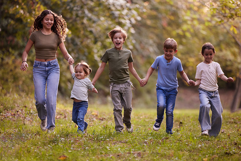 Fünf Kinder im unterschiedlichen Alter halten sich an den Händen und laufen über eine Wiese.