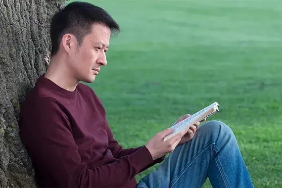 Junger Mann in ein Buch vertieft am Baum gelehnt