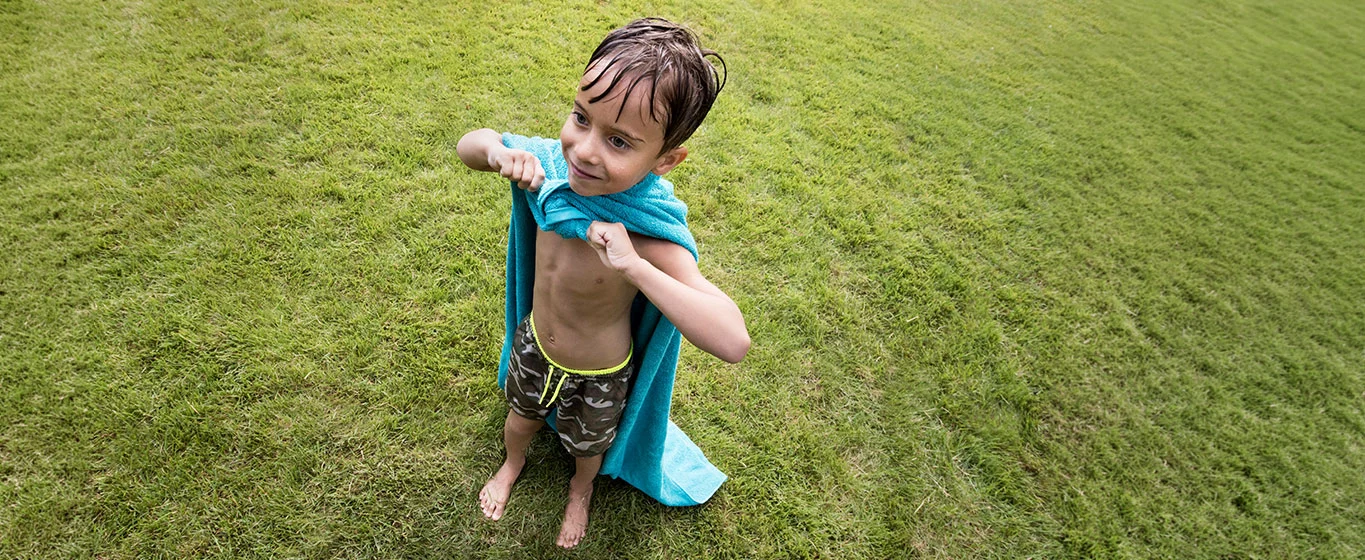 Kind spielt draussen mit einem Handtuch auf dem Gras