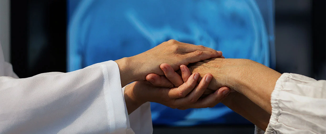 Ärzte untersuchen die Hand eines Patienten, im Hintergrund ein Gehirnscan.