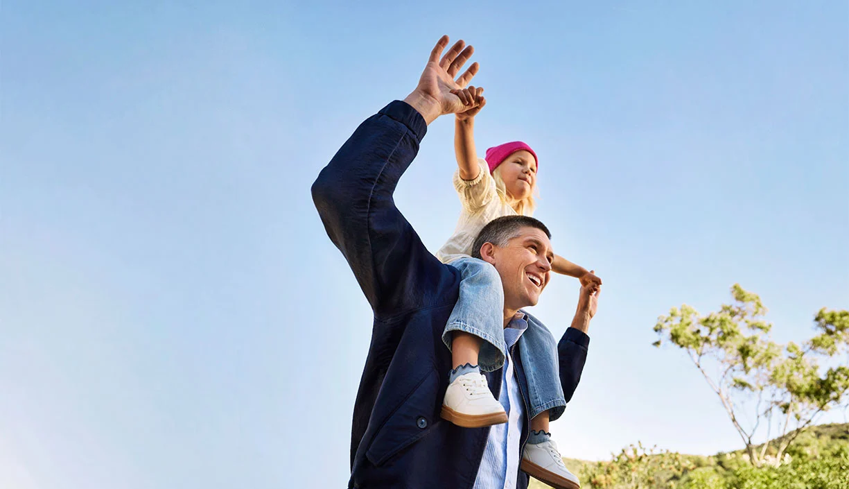 Glücklicher Vater mit Kind auf den Schultern unter blauem Himmel