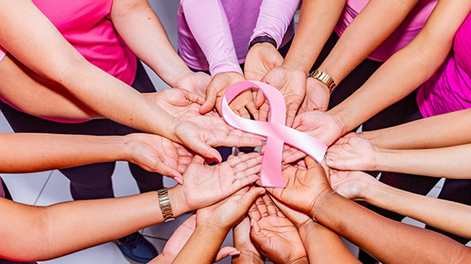 Viele Hände liegen kreisförmig übereinander und halten gemeinsam eine rosa Schleife