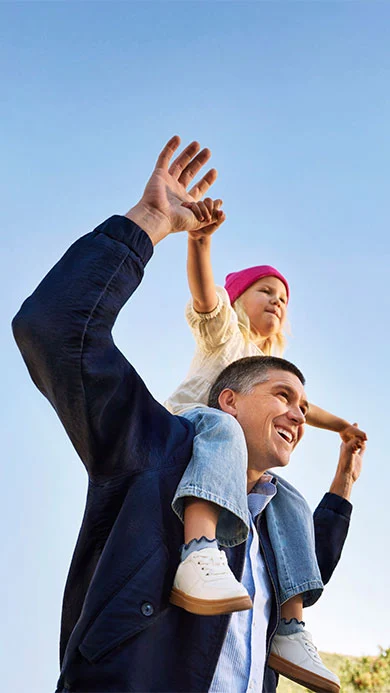 Glücklicher Elternteil mit Kind auf den Schultern unter klarem Himmel.