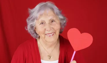 Mujer mayor sujetando un corazón de papel con fondo rojo