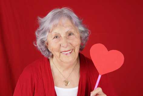 Mujer mayor sujetando un corazón de papel con fondo rojo