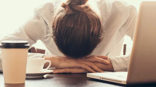 Mujer agobiada apoya su cabeza sobre sus manos frente al ordenador