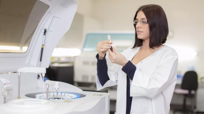 Mujer farmacéutica sujetando y observando una pipeta con un líquido dentro