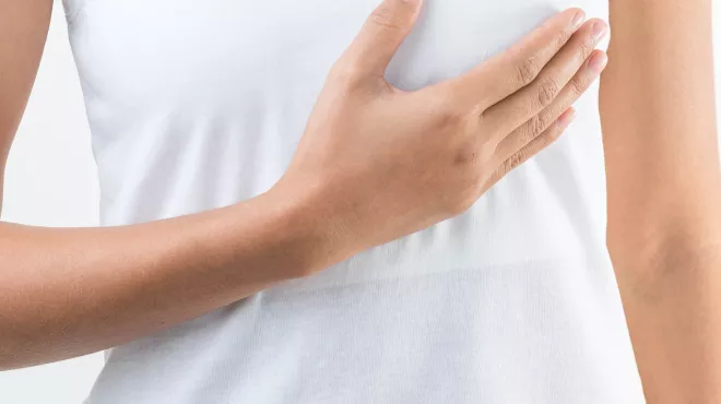 mujer con camiseta blanca tocando su pecho izquierdo con su mano derecha