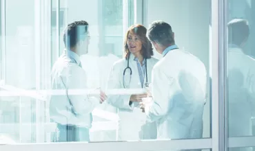 Kolme valkotakkista lääkäriä keskustelemassa lasisella käytävällä
