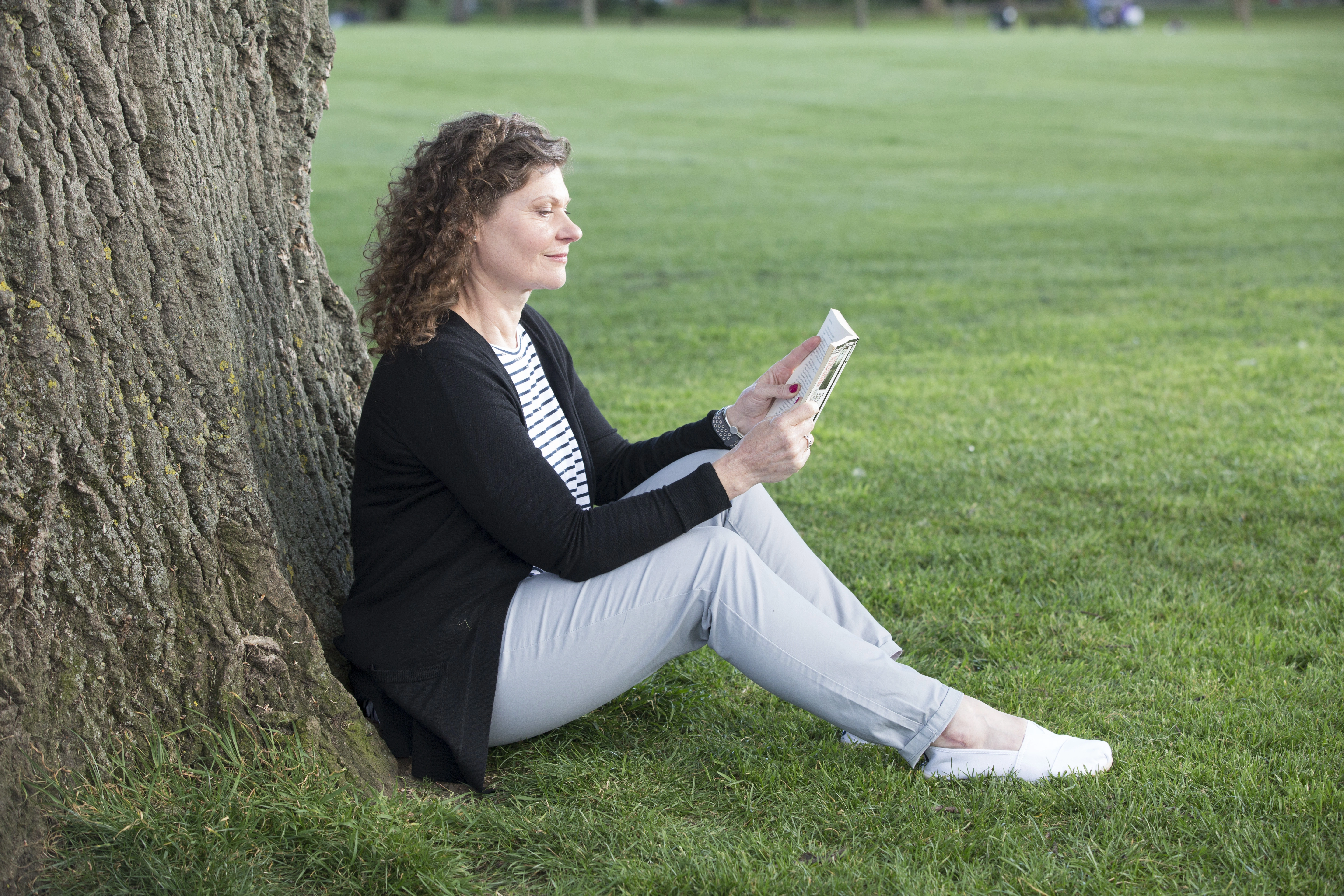 Nainen lukee kirjaa puun alla