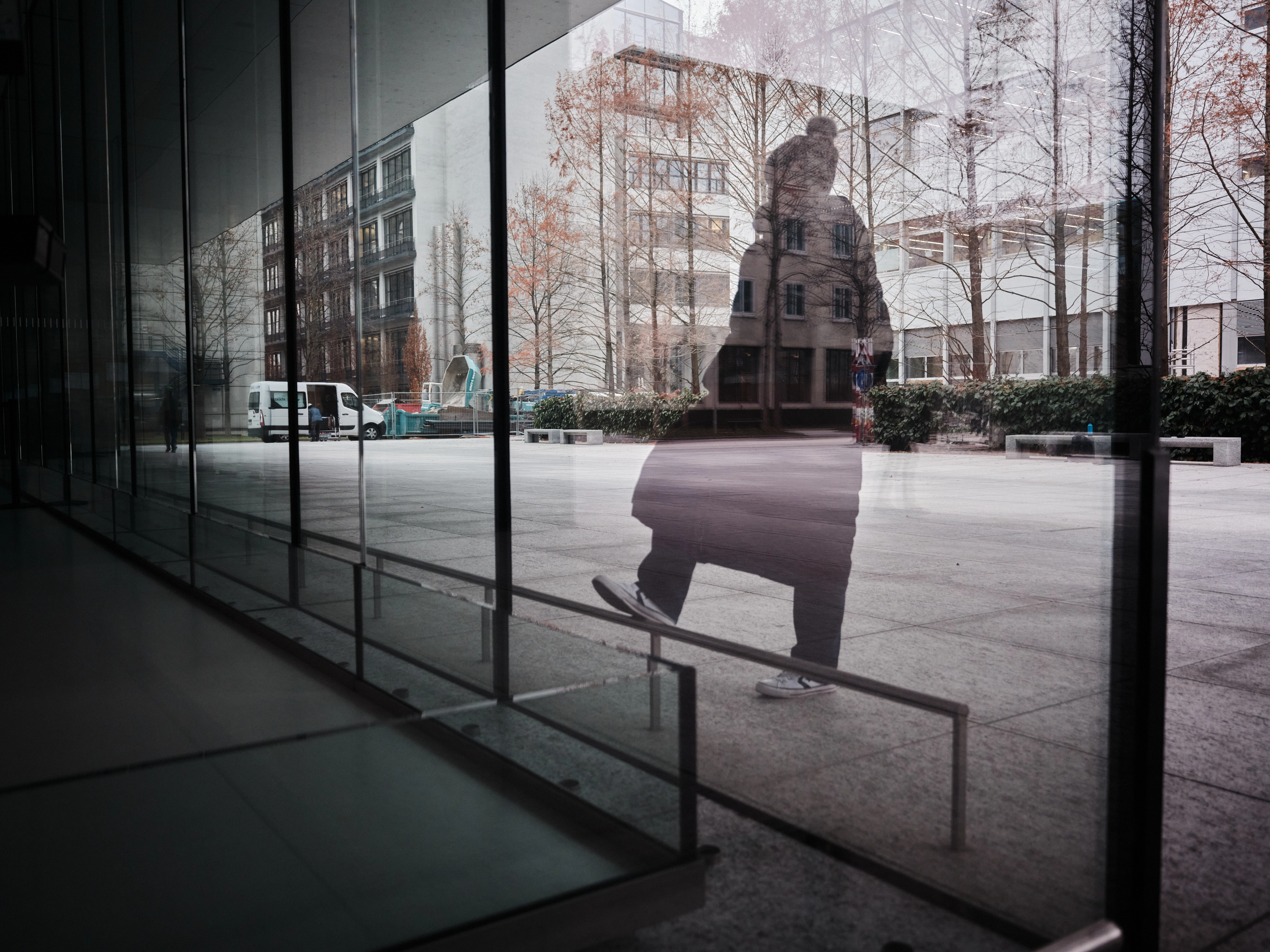 Talvitakkisen henkilön heijastus lasiseinästä