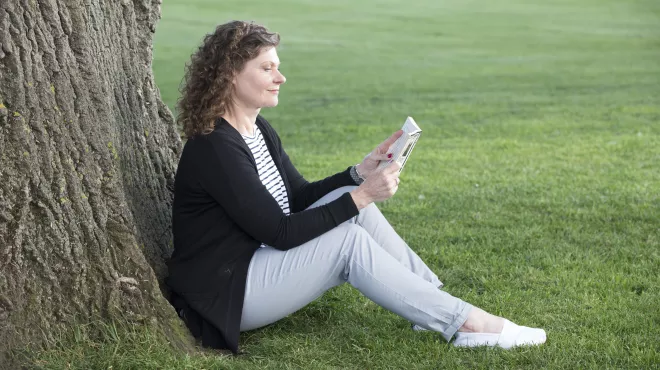 Nainen lukee kirjaa puun alla