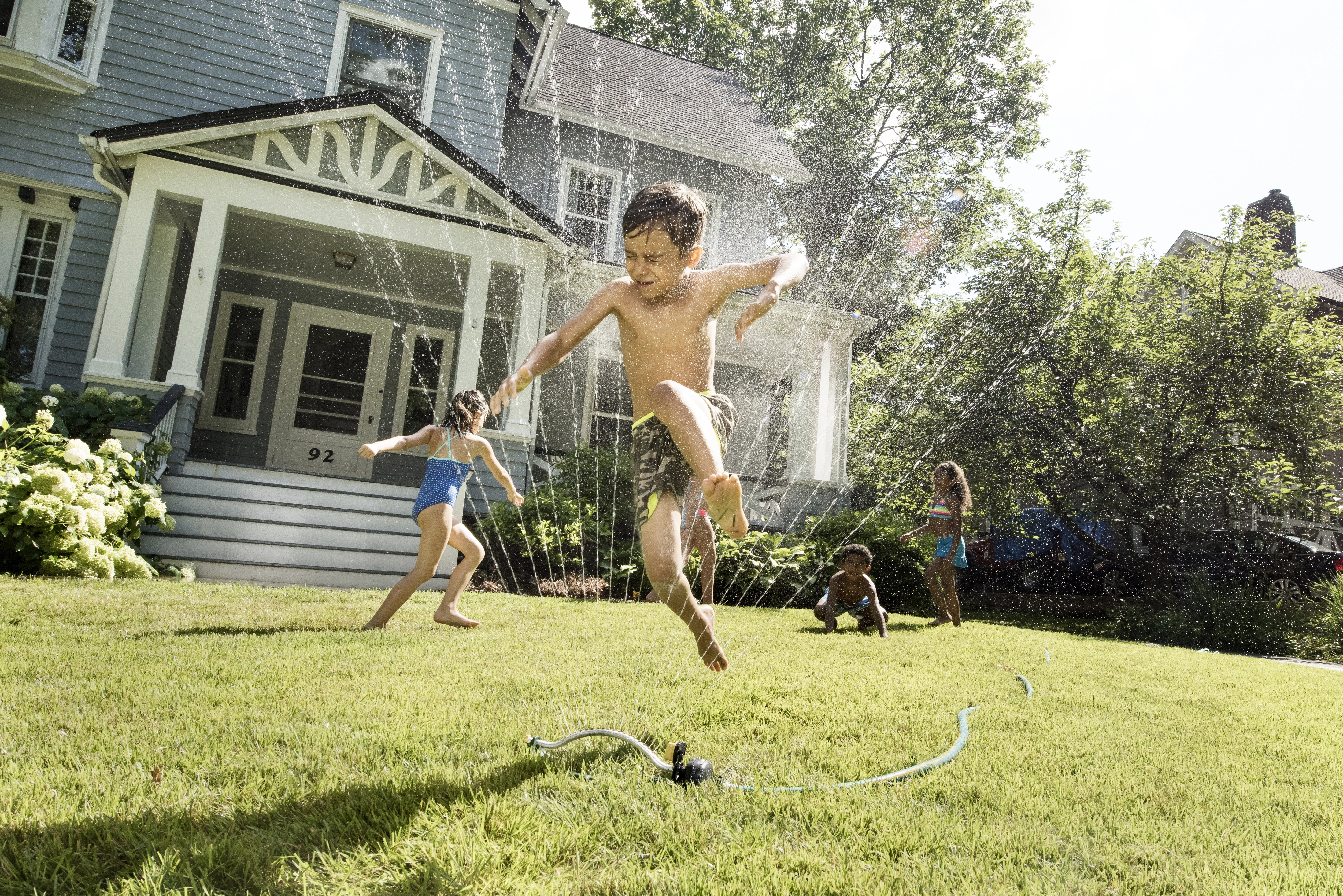 Kids playing joyfully with water sprays in front yard