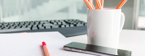 Tastatūra, telefons un zīmuļi uz galda