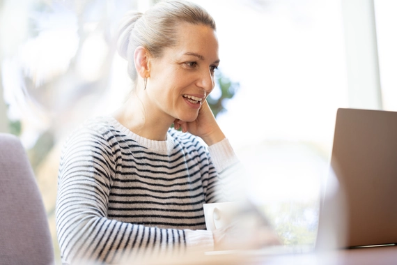 Smaidoša jauna sieviete, kas strādā pie datora