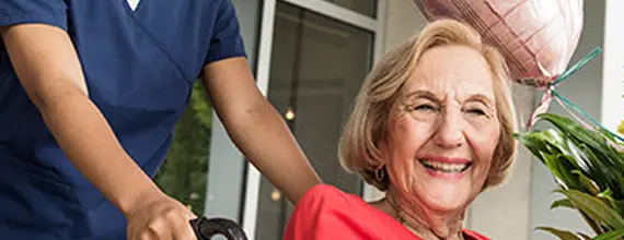 Zorgverlener duwt rolstoel met daarin een lachende patient