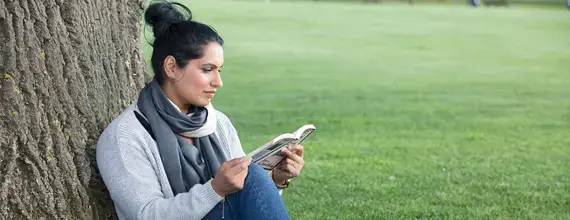 Vrouw zit tegen een boom en leest boek 