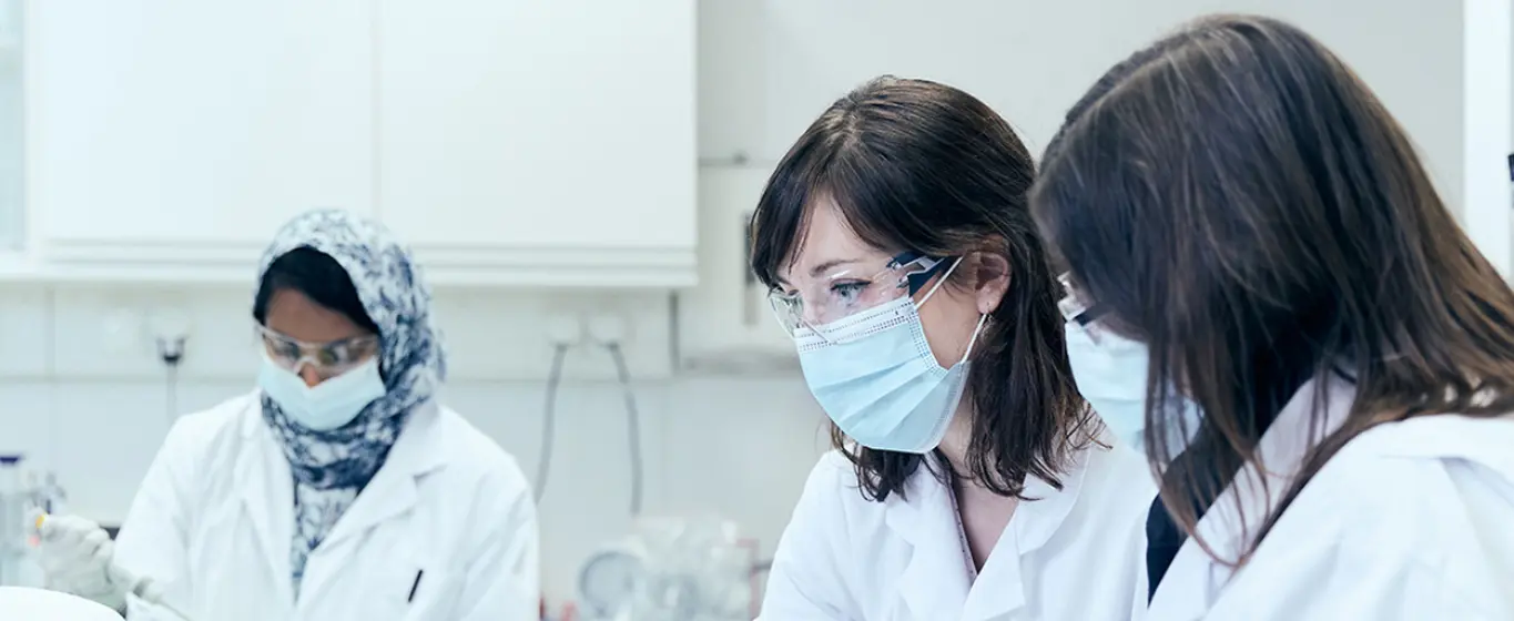 Cercetătoare care analizează date și eprubete în laborator