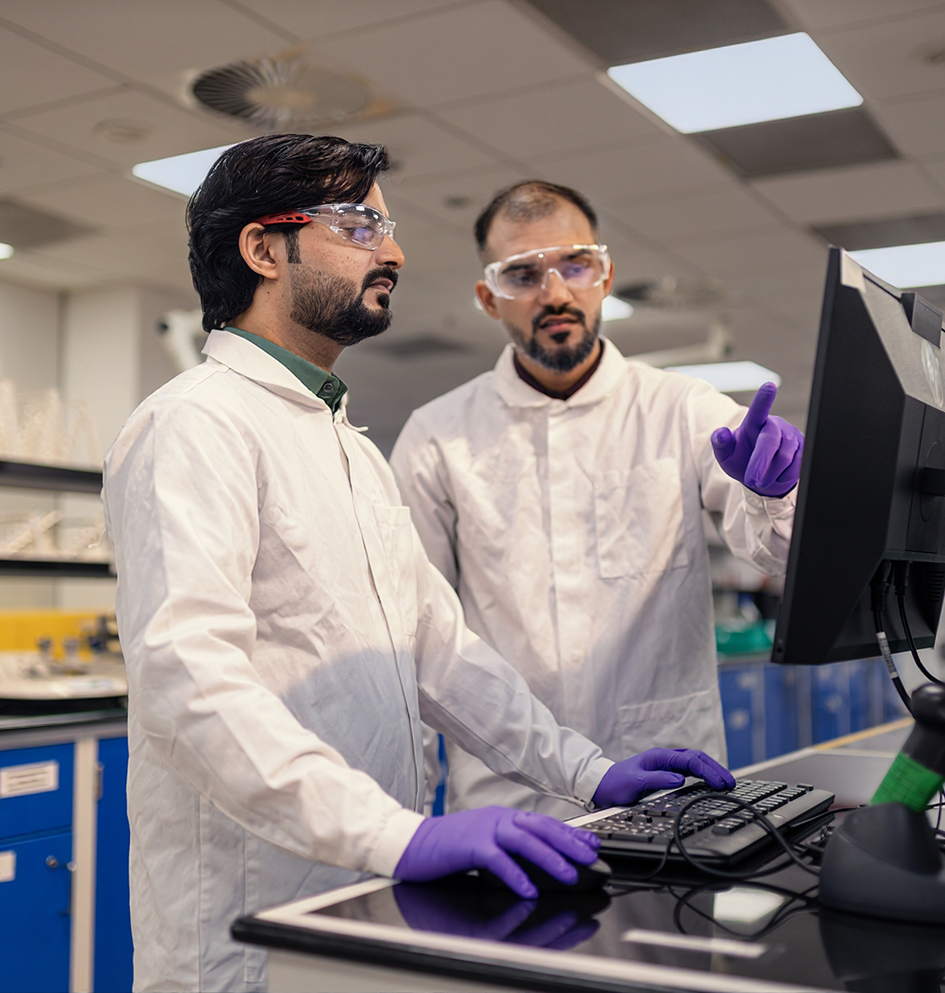 Two scientists work on a computer in a laboratory setting.