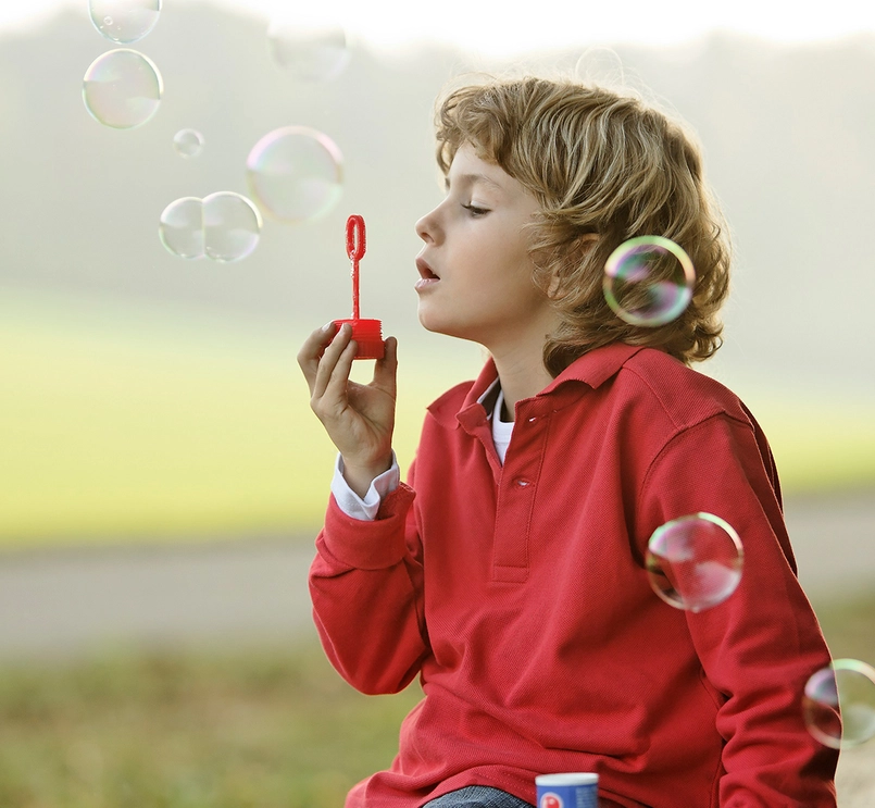 Ett barn blåser såpbubblor utomhus. Foto.