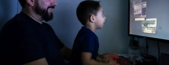 En far och en son sitter framför en dator. Foto.