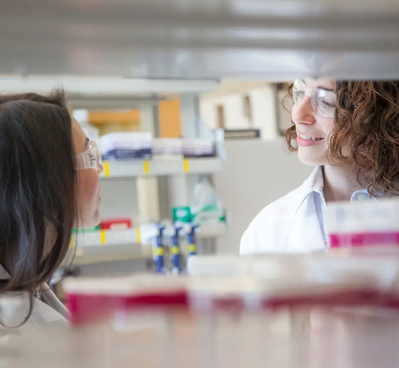 Two female scientists in lab coats talking in a laboratory