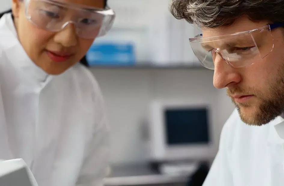 Two scientists in safety glasses analyzing data in a lab