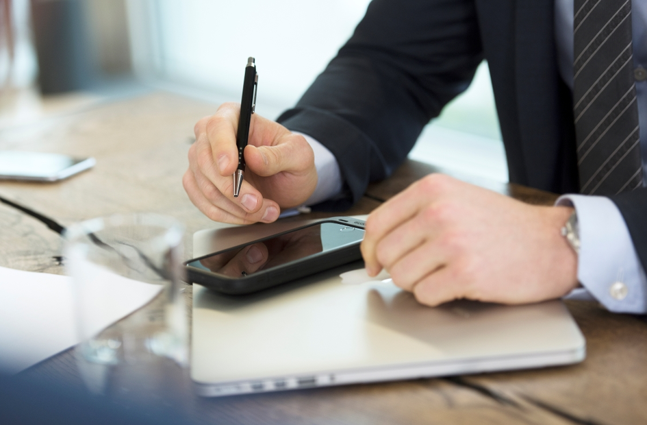 Businessman holding a pen over a smartphone and laptop