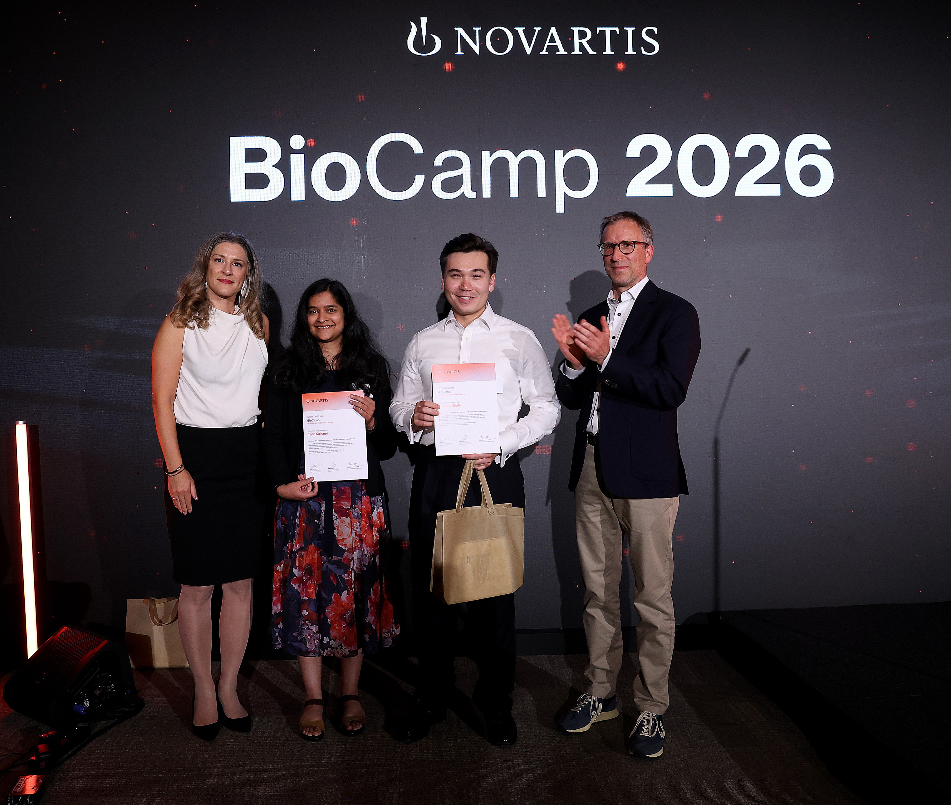 BioCamp winners holding certificates with event organizers in front of the BioCamp backdrop